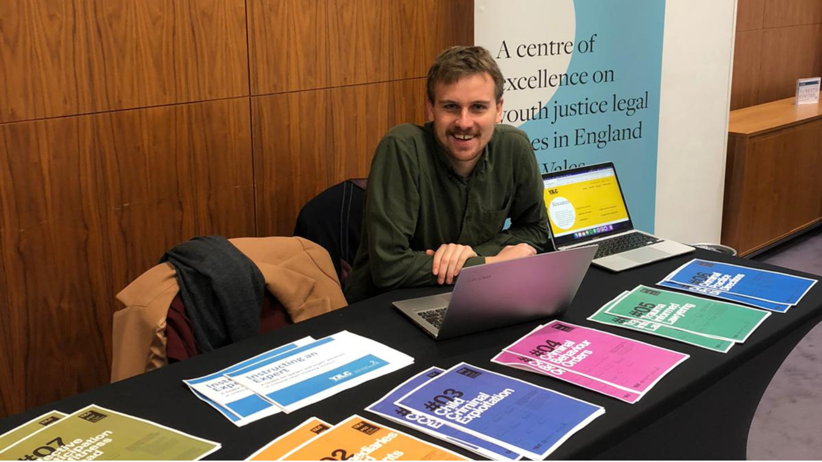 Robbie, wearing a green shirt, seated at a table with printed handouts in front of him.